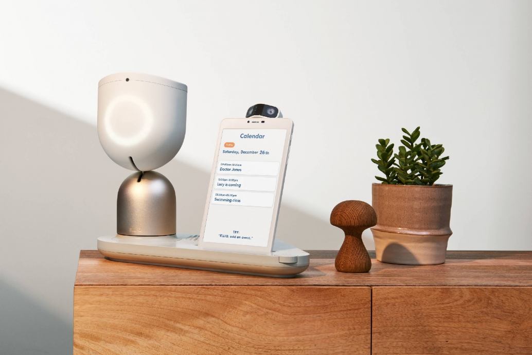 picture of ElliQ care robot for the elderly, the bedside table has a small robot and a screen with reminders for daily activities, such as taking medicine.