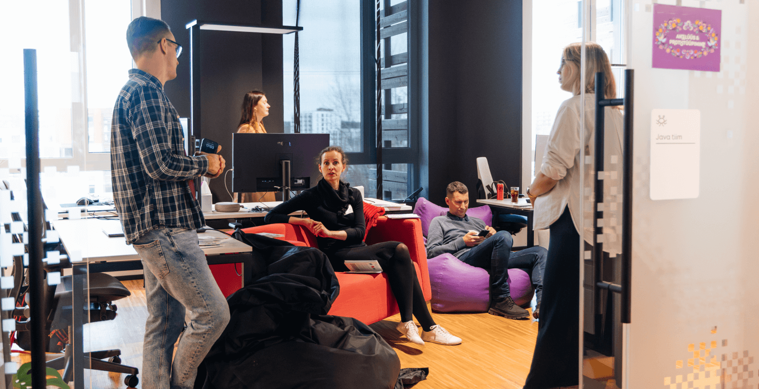 Five people are interacting in an office space, some sitting on beanbags and others standing, creating a relaxed and collaborative atmosphere.