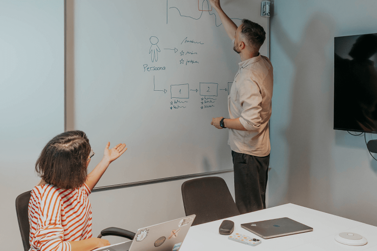 meie kaks kasutajakogemuse disainerit: meesterahvas tahvli ees skeemi joonistamas ja naisterahvas laua taga