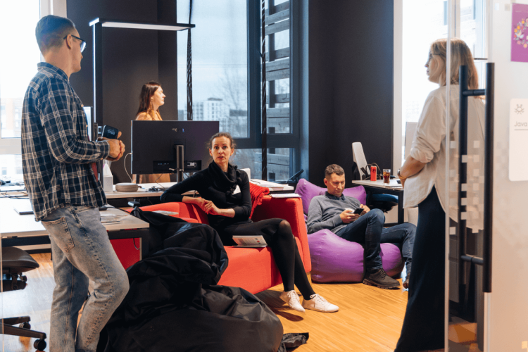 Five people are interacting in an office space, some sitting on beanbags and others standing, creating a relaxed and collaborative atmosphere.